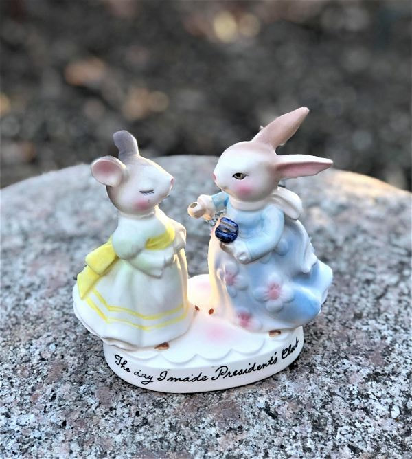 Bunny in blue dress presenting a pin or key to mouse in yellow dress